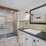 A nicely furnished bathroom interior with a glass door shower and a horizontal, long mirror by the sink